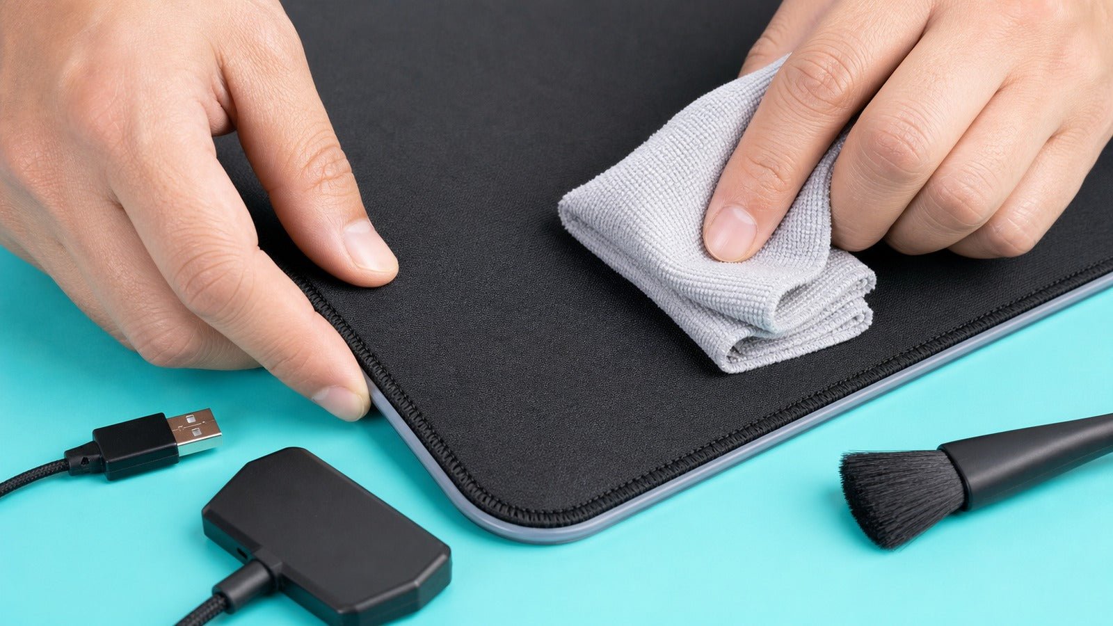 Hands cleaning an unplugged RGB desk mat with a microfiber cloth and soft brush