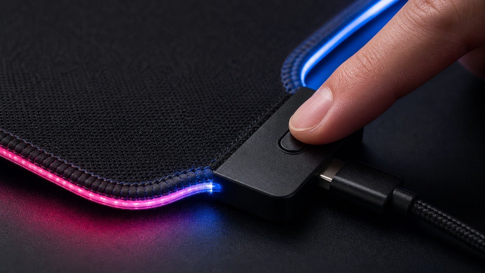 Macro view of an RGB desk mat's woven edge, light pipe, controller, and USB connection